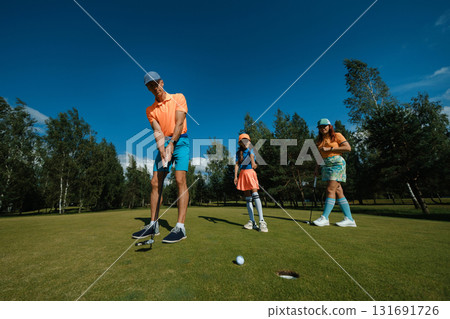 Family enjoys a fun day of golfing together on a sunny afternoon at a beautiful green course surrounded by trees 131691726