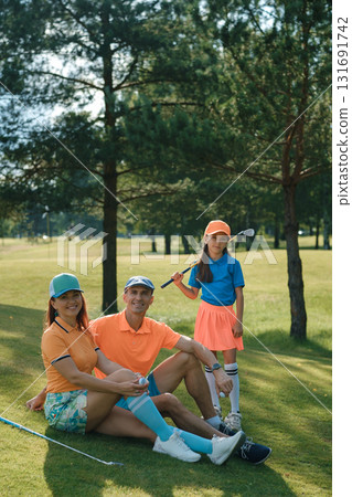 Family enjoys a sunny day playing golf together on a lush green course in the afternoon Family enjoys a sunny day playing golf together on a lush green course in the afternoon 131691742
