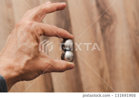 A man's hand holds two CNC metal spheres in warm daylight. A symbol of Earth's poles and the power to control their balance. Precision meets metaphor. 131691908