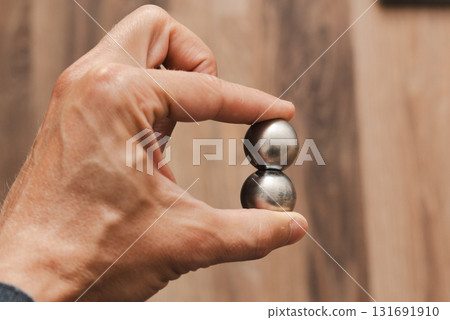 A man's hand holds two CNC metal spheres in warm daylight. A symbol of Earth's poles and the power to control their balance. Precision meets metaphor. A man's hand holds two CNC metal spheres in warm daylight. A symbol of Earth's poles and the power to control their balance. Precision meets metaphor. 131691910
