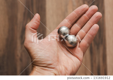 A man's hand holds two CNC metal spheres in warm daylight. A symbol of Earth's poles and the power to control their balance. Precision meets metaphor. 131691912