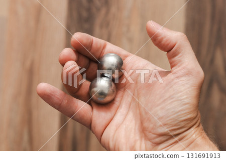 A man's hand holds two CNC metal spheres in warm daylight. A symbol of Earth's poles and the power to control their balance. Precision meets metaphor. A man's hand holds two CNC metal spheres in warm daylight. A symbol of Earth's poles and the power to control their balance. Precision meets metaphor. 131691913