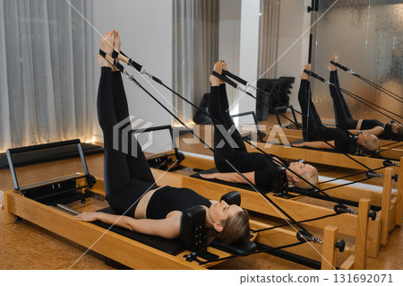 Woman practicing Pilates using reformer equipment in a bright studio during a midday session focusing on core strength and flexibility Woman practicing Pilates using reformer equipment in a bright studio during a midday session focusing on core strength and flexibility 131692071