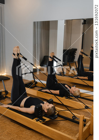 Pilates session showcasing two individuals performing leg exercises on reformers in a modern fitness studio 131692072
