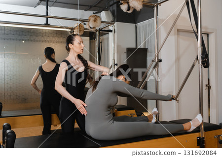 Pilates instructor guiding student on reformer machine during a private session in a modern studio Pilates instructor guiding student on reformer machine during a private session in a modern studio 131692084