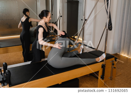 Pilates instructor guides student through reformer exercise in a bright studio setting focusing on flexibility and strength training 131692085
