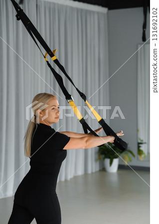 Woman performing resistance training using suspension straps in a modern fitness studio during a workout session 131692102