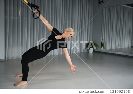 Fitness enthusiast performs suspension training exercise in a spacious studio with natural lighting during a workout session focused on strength and balance 131692108