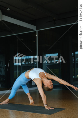 Yoga practitioner performs an advanced pose in a stylish training studio with floor-to-ceiling windows letting in natural light Yoga practitioner performs an advanced pose in a stylish training studio with floor-to-ceiling windows letting in natural light 131692150