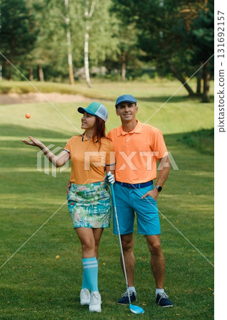 Couple enjoying a sunny afternoon playing golf on a lush green course, showcasing vibrant outfits and a sense of fun during their leisure activity 131692157
