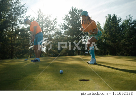 Golfers enjoying a sunny afternoon on a beautifully manicured course, celebrating a successful putt while surrounded by lush trees and greenery 131692158