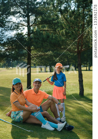 Family enjoys a sunny day of golfing together at a beautiful outdoor golf course while showcasing their stylish outfits and fun energy Family enjoys a sunny day of golfing together at a beautiful outdoor golf course while showcasing their stylish outfits and fun energy 131692178