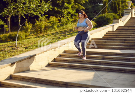 Young overweight woman in sportswear running down stone steps in city park in morning 131692544