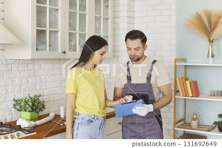Houswife and worker standing in kitchen wearing overall discussing, professional service for repair Houswife and worker standing in kitchen wearing overall discussing, professional service for repair 131692649