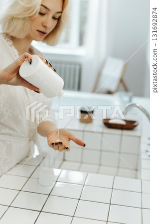 Pouring shampoo from bottle on female hand in bathroom. 131692874