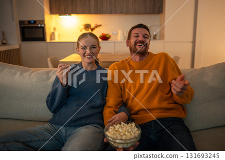 Happy laughing couple enjoying film together, eating popcorn and smiling. Weekend bonding ritual Happy laughing couple enjoying film together, eating popcorn and smiling. Weekend bonding ritual 131693245