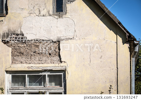 Old abandoned house with cracked plaster, peeling paint, and weathered wooden window frames 131693247
