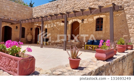 Sunny courtyard of a traditional Mediterranean stone house with flowering pots 131693249