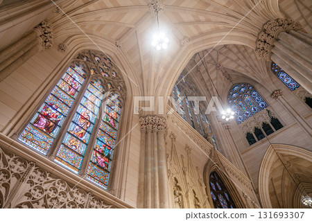 A close-up view of vibrant stained glass windows inside a Gothic-style cathedral. The arched stone architecture and ornate ceiling enhance the sacred and artistic ambiance of the space. A close-up view of vibrant stained glass windows inside a Gothic-style cathedral. The arched stone architecture and ornate ceiling enhance the sacred and artistic ambiance of the space. 131693307