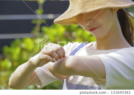 A woman who seems to be itchy after being bitten by an insect while gardening 131693361