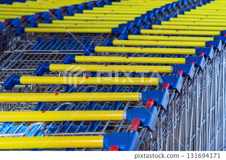 Neatly arranged rows of shopping carts with yellow handles and blue details. Concept of shopping, retail, organization, commerce and consumerism Neatly arranged rows of shopping carts with yellow handles and blue details. Concept of shopping, retail, organization, commerce and consumerism 131694171