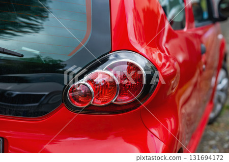 Closeup of red car rear with taillight reflection and smooth surface. Concept of modern transport, color design, automotive detail with glossy texture Closeup of red car rear with taillight reflection and smooth surface. Concept of modern transport, color design, automotive detail with glossy texture 131694172