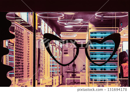 Modern eyeglass shop interior with heart-shaped frame on glass and neon lighting. Concept of glasses, fashion, and vision combining style and modern retail design 131694178