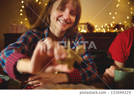 Smiling Woman In Plaid Shirt Decorating A Star-Shaped Cookie In A Cozy Holiday Kitchen With Warm Christmas Lights 131694229