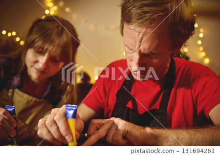 Family Craft Night With Friends: Two Adults Creating Art Under Warm Christmas Lights Family Craft Night With Friends: Two Adults Creating Art Under Warm Christmas Lights 131694261