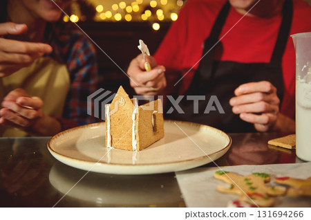 Gingerbread House Decoration With Friends In Cozy Kitchen During Christmas Festivities Gingerbread House Decoration With Friends In Cozy Kitchen During Christmas Festivities 131694266