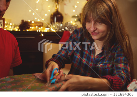 Woman in Plaid Shirt Wrapping Gifts by Christmas Lights, Sharing a Cozy Moment 131694303
