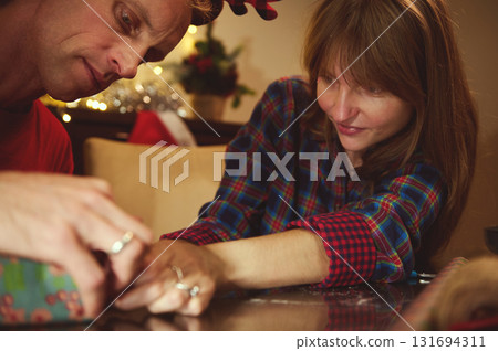 Family And Friends Share A Warm Christmas Gift Wrapping Moment At Home, Celebrating Togetherness With Festive Decor And Cozy Holiday Vibes 131694311
