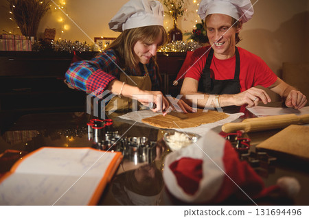 Family Friends Bake Holiday Cookies Together in a Cozy Kitchen, Wearing Chef Hats Under Christmas Lights 131694496