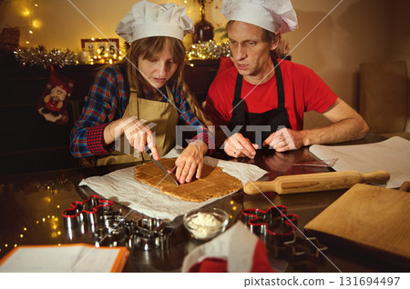 Family Cooks in Festive Kitchen Wearing Chef Hats, Rolling Dough and Cutting Cookies for Christmas Celebration Family Cooks in Festive Kitchen Wearing Chef Hats, Rolling Dough and Cutting Cookies for Christmas Celebration 131694497