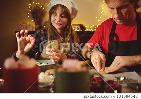 Family Baking Scene: Woman In Chef Hat And Man In Apron Creating Festive Treats In A Cozy Kitchen 131694548