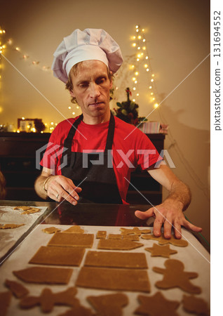Chef in Red Shirt and Black Apron Shapes Gingerbread Cookies for Christmas in Cozy Home Kitchen 131694552