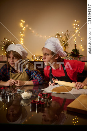 Family Chefs In Chef Hats Rolling Dough At Festive Kitchen With Warm Fairy Lights 131694587