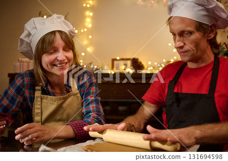 Happy Friends Baking Together in a Cozy Kitchen with Chef Hats, Rolling Dough, and Holiday Lights Happy Friends Baking Together in a Cozy Kitchen with Chef Hats, Rolling Dough, and Holiday Lights 131694598