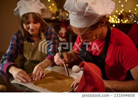 Cooking Friends Create Holiday Joy As Chefs Roll Dough And Cut Gingerbread Shapes By Cozy, Warm Lights Cooking Friends Create Holiday Joy As Chefs Roll Dough And Cut Gingerbread Shapes By Cozy, Warm Lights 131694608