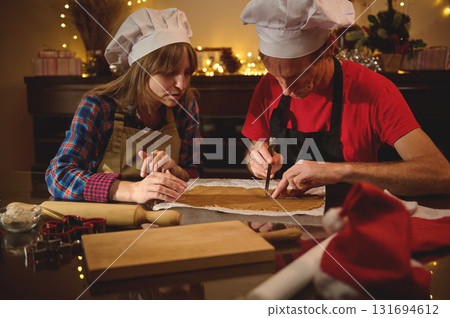 Cooking Duo in Chef Hats Rolling Dough Together for Christmas Treats in a Cozy Kitchen 131694612