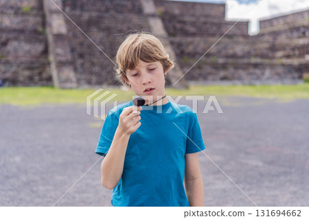 Boy tourist holding and observing a piece of obsidian in front of Teotihuacan pyramids, Mexico, symbolizing cultural discovery, archaeology, and educational travel Boy tourist holding and observing a piece of obsidian in front of Teotihuacan pyramids, Mexico, symbolizing cultural discovery, archaeology, and educational travel 131694662