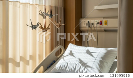 Colorful origami paper cranes mobile hanging above hospital bed with medical equipment in patient room interior 131695916