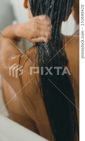 A woman washes her hair in a peaceful bath, surrounded by flowing water and a tranquil ambiance 131698420