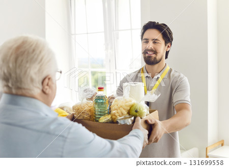 Happy volunteer guy giving food box to elderly man, close-up Happy volunteer guy giving food box to elderly man, close-up 131699558