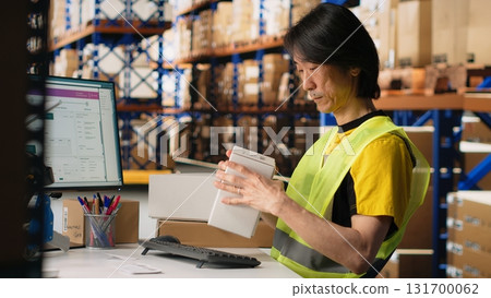 Distribution hub staff printing and applying awb labels on packages, wearing hi vis vest in a storehouse. Using barcode airway bill and shipping labels for order fulfillment and tracking. Camera B. Distribution hub staff printing and applying awb labels on packages, wearing hi vis vest in a storehouse. Using barcode airway bill and shipping labels for order fulfillment and tracking. Camera B. 131700062