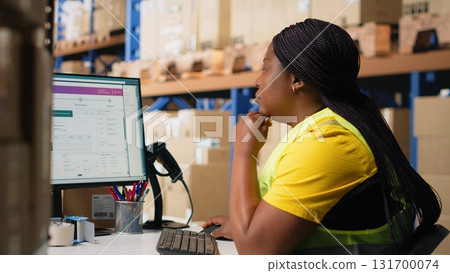 Warehouse employee using package tracking software on computer monitor, managing express delivery and using awb tracking info to update real time parcel status. Distribution hub. Camera B. 131700074