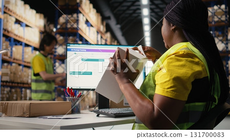 African american staff works on packages labeling for express delivery, ensuring accurate package tracking with a professional software. Worker processing orders in stock room. Camera A. 131700083