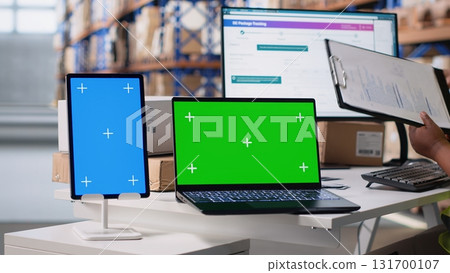 Multiethnic team of warehouse workers next to green screen monitor. Managing shipping labels, barcode scanner data or e-commerce inventory tracking systems in industrial warehouse. Camera B. 131700107