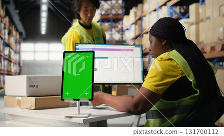 Warehouse employee in hi vis vest uses copy space display with technology of shipping software, packaging systems and inventory management tools. E-commerce logistics. Camera A. 131700112