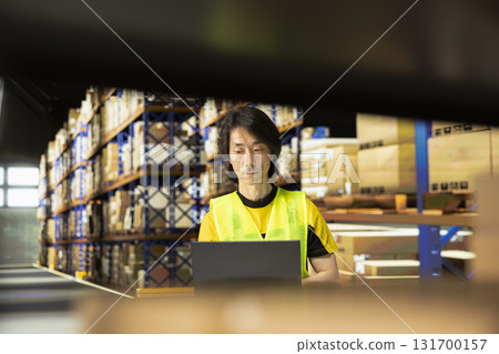 Warehouse employee in workwear preparing packages for local delivery, processing custom orders and handling merchandise within large business operation focused on e-commerce. Warehouse employee in workwear preparing packages for local delivery, processing custom orders and handling merchandise within large business operation focused on e-commerce. 131700157